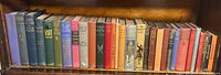 Full view of 30 vintage hardcover decorative books on a wood bookshelf showing various colors and titles
