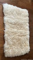 Full view of rectangular cream-colored curly lambskin wool rug laid flat on wooden floor, showing texture and natural shape.