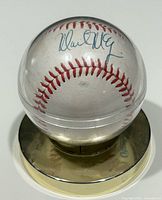 Front view of the autographed baseball in clear sphere on gold base showing Mark McGwire's signature in blue ink.