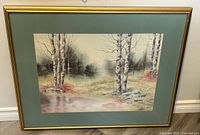 Full view of the framed watercolour painting showing birch trees, water, and misty woods with golden frame and green mat.