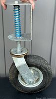 Front view of pneumatic spring-loaded caster showing blue spring, metal bracket, and pneumatic rubber tire.