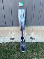 Full view of Pro Point Large Propane Torch Kit in original sealed plastic package leaning against wall outside on grass.