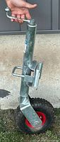 Side view of metal swivel trailer jack with crank handle, attached pneumatic tire, showing handle and latch mechanism.