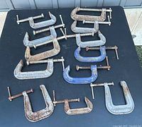 Overview of 12 vintage C-clamps laid out on black surface, various sizes, mostly metal with rust and patina, several marked 'EXTRA STRONG'.