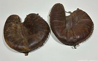 Two vintage leather catchers gloves side by side showing worn leather surfaces and lacing.