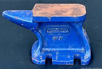 Front side view of vintage Record #11 anvil showing blue painted cast metal body with embossed branding and wooden top face.