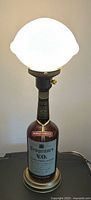 The lamp turned on, showing illuminated white glass shade and base made from Seagram's V.O. Canadian Whisky bottle with brass fittings.