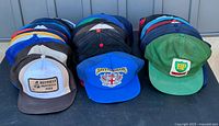 Collection of 36 vintage snap back ball caps arranged in rows showing front logos including BP, Restoule Provincial Park, and others