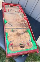 Top-down angled view of vintage wooden tabletop hockey game showing playing surface, red and green painted trim, metal pegs and levers, and goal with woven net.