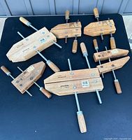 Six wooden hand screw clamps laid out on a black surface, varying sizes and wooden handles visible.