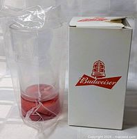 Glass Budweiser cup inside protective plastic with box beside it displaying Budweiser logo.