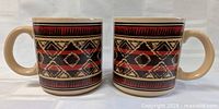 Front side of two ceramic coffee mugs with southwestern geometric patterns in red, black, beige.