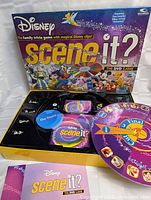 Opened game box showing inside components including DVD, question cards, player tokens, and spinner.