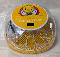 Photo showing top view of the TrioCottage egg incubator with transparent dome, yellow base, and cartoon chick illustration on top.