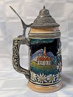 Front view of vintage German lidded beer stein showing house, flowers, and ornate lid.