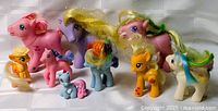 Photo of nine My Little Pony toy dolls arranged in two rows on a white surface, showing details of colors, mane and tail styles.