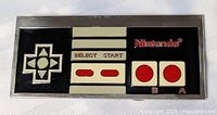 Front view of the NES controller themed belt buckle showing details of the directional pad, buttons, and logo.