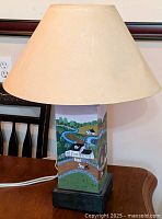 Full view of the tole painted table lamp showing one painted side with off-white fabric lampshade
