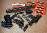 Overview of lot showing multiple curved and straight track sections, two turnouts, girder bridge, open box of track and five red train car boxes