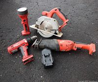 Group shot of five Milwaukee cordless tools and one battery pack on asphalt