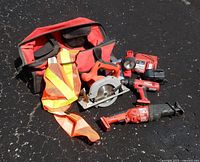 All tools, battery, charger, bag and safety vest laid out on pavement
