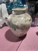 Photo of a Chinese ceramic vase showing a crane bird in flight with bamboo and cloud motifs on its surface, placed on a table with decorative background items.