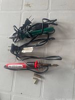 Photo showing two wood burning tools with power cords and two copper tips, placed on a textured surface.