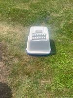 Top view of one extra large covered cat litter box placed on grass, showing light gray cover with ventilation slots and a handle