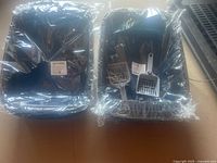 Four black plastic cat litter boxes, each individually wrapped in plastic with a grey plastic litter scoop included in packaging.