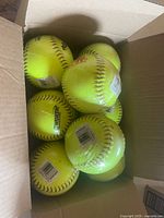 Box containing eight yellow softballs wrapped in clear plastic, showing the lot is new and unused.