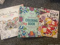 Front view of three adult coloring books: Nature's Beauty Coloring, Chill & Unwind Coloring Book, and Challenging Color by Number book with colorful floral covers.