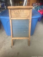 Front view of mini washboard showing wood frame and blue metal scrubbing surface with branding.