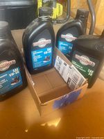 Four bottles of Motomaster oil for snowblower and lawnmower seen in cardboard box on wood floor.