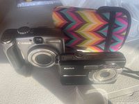 Front view of Canon PowerShot A710 and Kodak EasyShare M753 cameras with colorful camera case behind them.