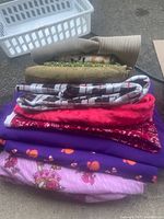Stack of various folded fabrics including plaid, bandana, printed, and solid colors, totaling 15-20 yards