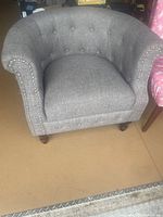 Front view of the grey fabric club chair with rounded arms and button tufting, showing overall design and condition.