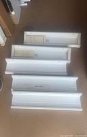 Five Ikea Mosslanda shelves laid out on the floor, two are still in original packaging and three are used with visible minor wear marks.