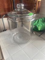 Photo of a large clear glass urn with lid placed on a white surface, with a green price sticker on the lid.