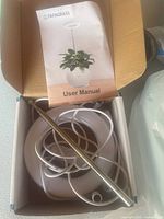 Open box showing mini LED grow lamp components: white base with flexible neck, USB power cable, and user manual titled 'FAFAGRASS User Manual' featuring photo of the lamp and a plant pot.