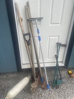 Photo of outdoor tools leaning against an exterior door including shovels, rakes, lawn aerators, and a duster.