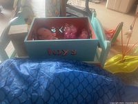 Blue wooden toy box filled with multiple pet toys, showing pink stuffed octopus and other toys inside.