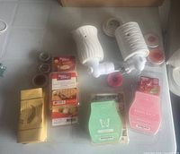 Photo showing two white ceramic wax burners and various scented wax melt packages laid out on a table, including Better Homes & Gardens and ScentSationals brands.
