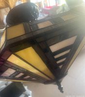 Close-up side angle of the stained glass light shade showing yellow and cream glass panels with dark metal framing and detailing.