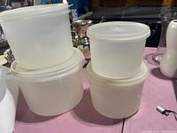 Four translucent white round Tupperware containers with lids shown stacked and arranged