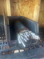 Welding rods bundled inside a black plastic container on a metal shelf with wooden walls in the background.