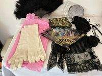 Photo showing antique ladies' accessories including long gloves, feathered fan, painted fan with lace, embroidered handbag, black lace scarf, mesh evening bag, and crocheted bag.