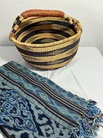 Photo showing handwoven basket with leather handle and lightweight blue patterned blanket