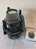 Front view of Bissell Spot Clean Pro portable carpet cleaner on white surface with quick start guide manual placed beside it.