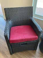Close-up view of one brown resin wicker-style chair with red cushion and slide-out ottoman