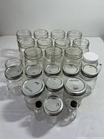 Front view of multiple canning jars arranged on a white surface including small bottles and jars with white and metal lids.